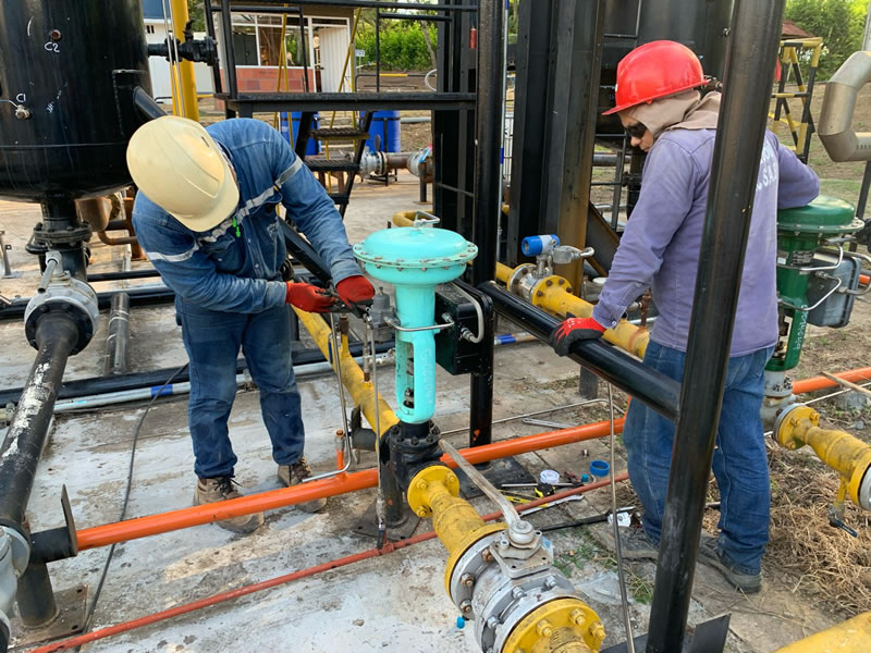 Técnicos con casco y guantes ajustando válvulas de control en una línea de proceso