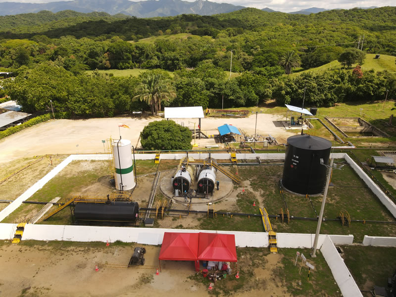 Vista aérea de una facilidad de producción con tanques, tuberías y cerramiento, rodeada de vegetación y montañas del Huila